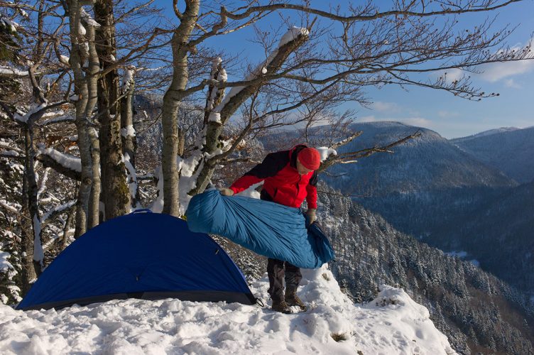 A camper preparing his sleeping bag on a snowy hill