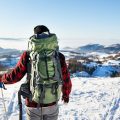 A man with backpack and cold weather hiking gear walking in the snow