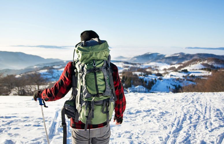 A man with backpack and cold weather hiking gear walking in the snow