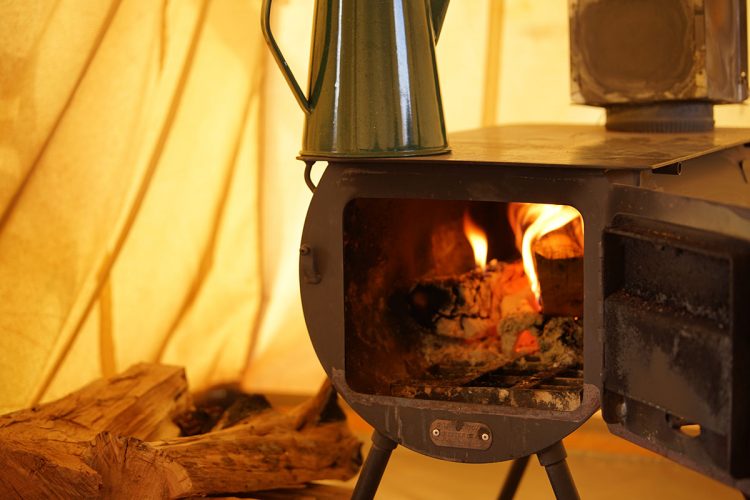 A wood burning tent stove, door open with a kettle on top